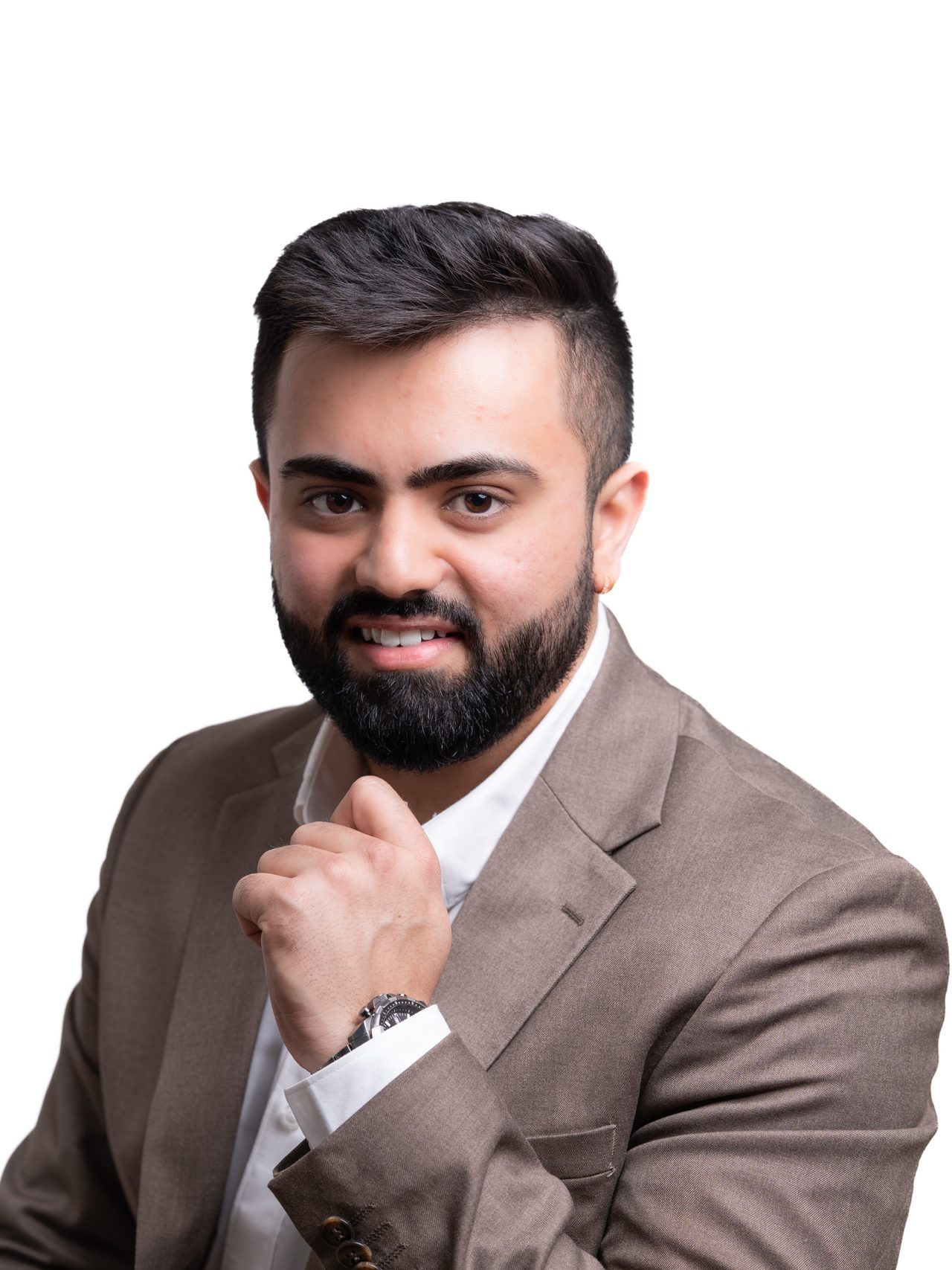 Studio headshot of a smiling bearded man in a brown blazer with his hand at his chin, on a white background.